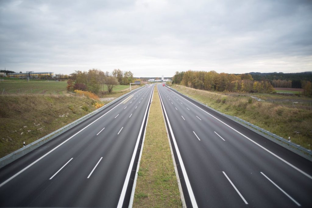 landscape-clouds-trees-outside-967072 A serene image of an empty highway stretching through a peaceful countryside under a cloudy sky.
